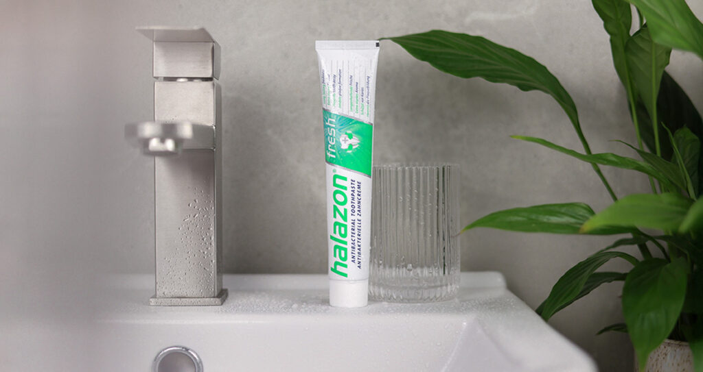 Die Zahnpasta Halazon fresh steht neben einem Glas auf einem modernen Waschbecken für optimale Mundpflege.