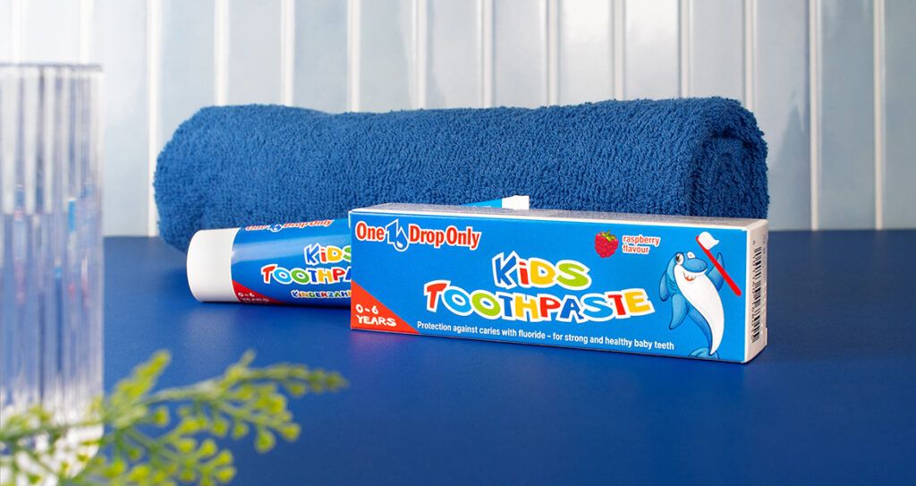 Eine Kinderzahnpasta von One Drop Only liegt neben einem blauen Handtuch auf einem Tisch für optimale Mundhygiene.
