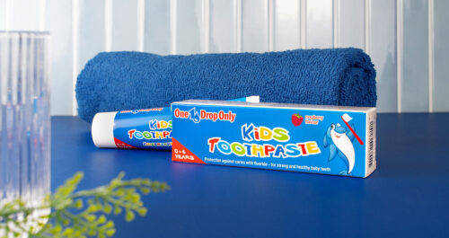 Eine Kinderzahnpasta von One Drop Only liegt neben einem blauen Handtuch auf einem Tisch für optimale Mundhygiene.