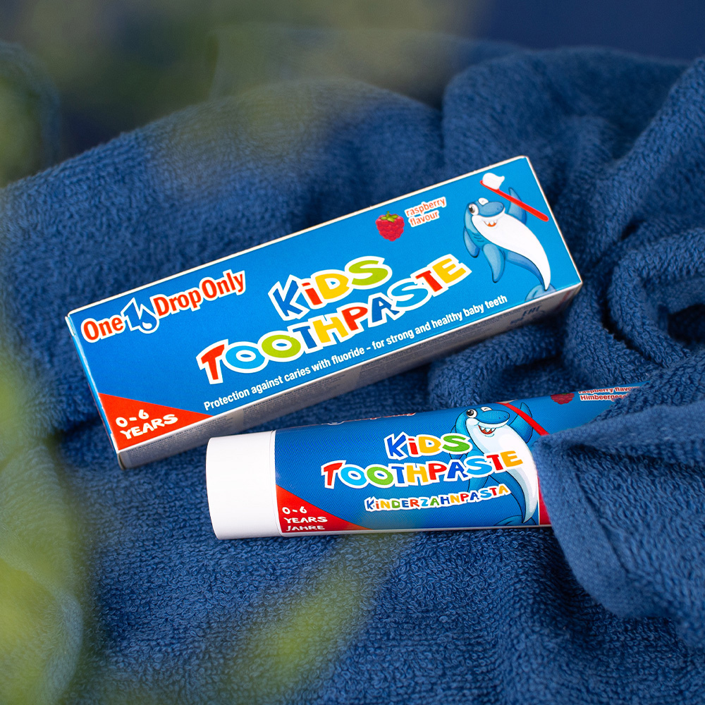 Die Tube Kinderzahnpasta von Onedroponly liegt auf einem blauen Handtuch, ideal für tägliche Mundpflege.
