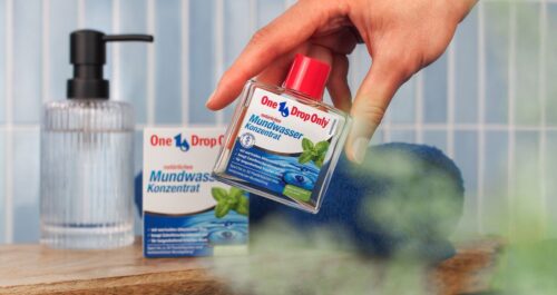 Eine Hand greift nach einer Flasche One Drop Only Mundwasser, ideal für effektive Mundhygiene und frischen Atem.