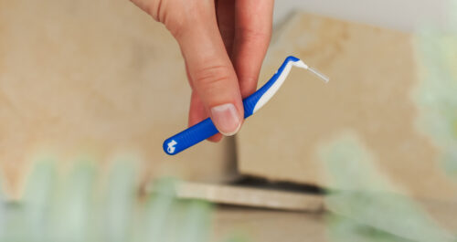 Eine Hand hält eine blaue Interdentalbürste für effektive Mundhygiene von One Drop Only.