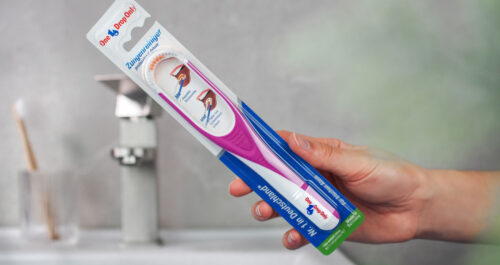 Eine Hand hält einen Onedroponly Zungenreiniger in der Verpackung zur Förderung der Mundhygiene.