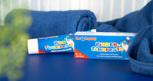 Eine Tube Kinder-Zahnpasta von One Drop Only liegt auf einem blauen Handtuch, betont durch den KZC_Header_de-web.