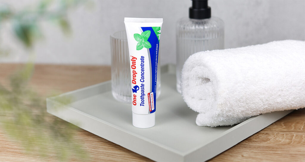A tube of One Drop Only toothpaste concentrate rests on a tray beside a glass and a towel, highlighting effective Mundpflege.